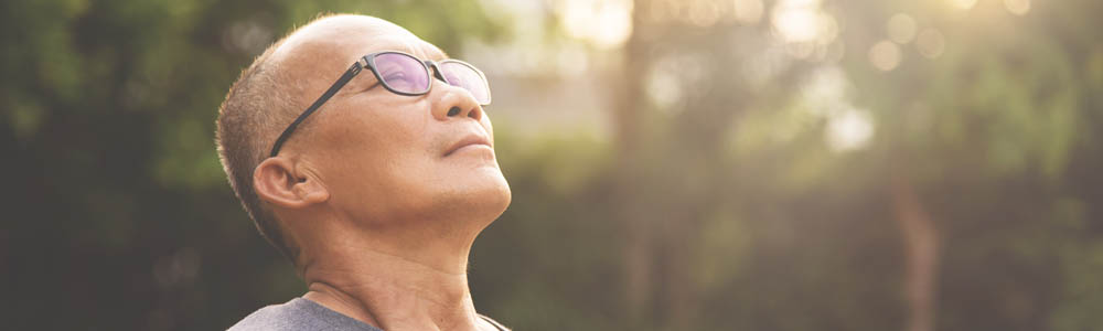 Older man leaning back so his face is point towards the sun, the background is blurred trees Older man leaning back so his face is point towards the sun, the background is blurred trees
